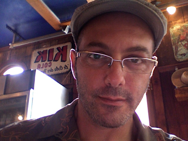 La solitude du photographe. 1 Portrait de Stéphane Najman alias Photoman, en casquette et lunettes dans un café