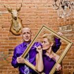 Photo booth Alliance Vivafilms : couple en violet posant avec un cadre doré devant un mur de briques